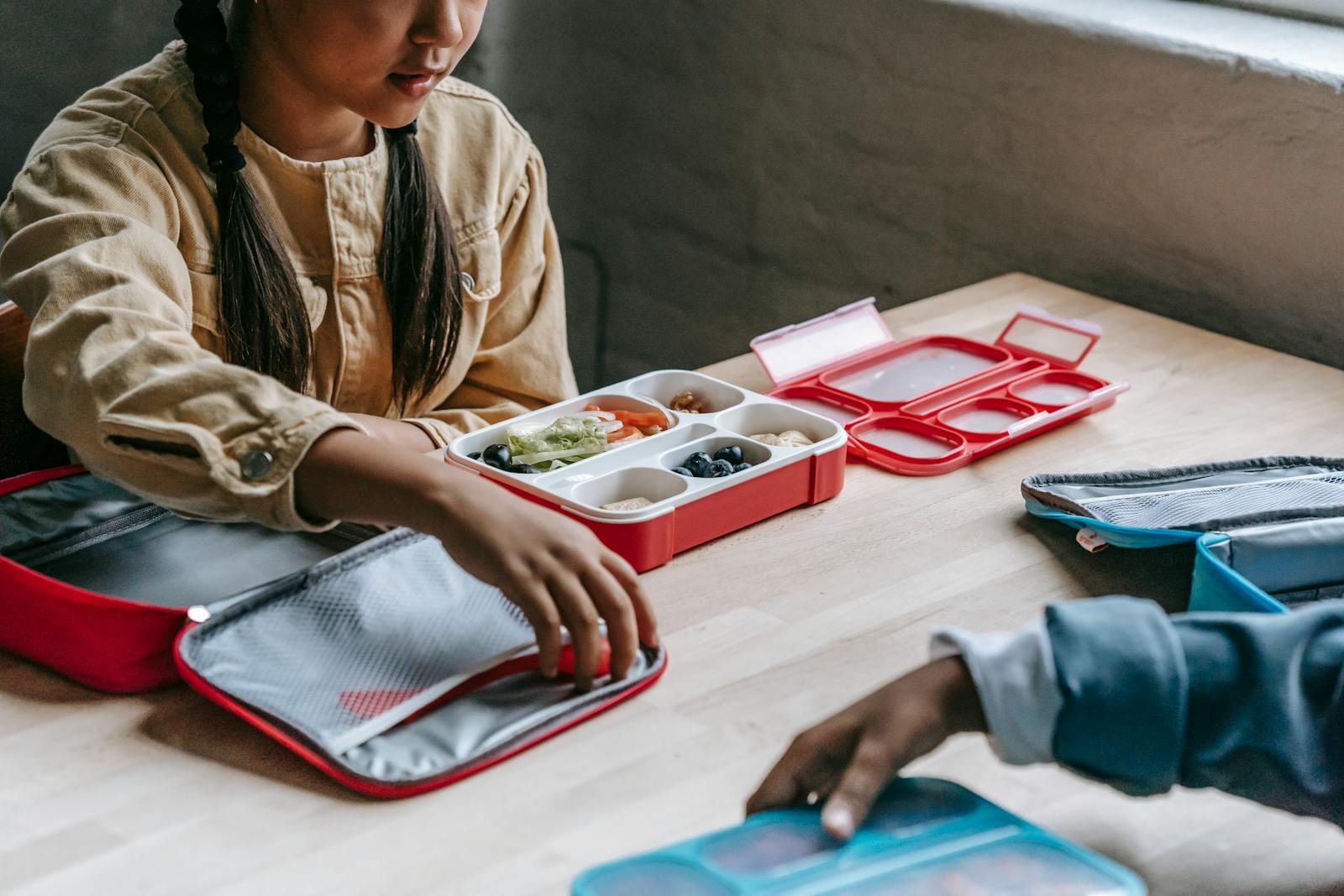 From above of crop anonymous ethnic schoolkids with lunch boxes full of delicious food in classroom